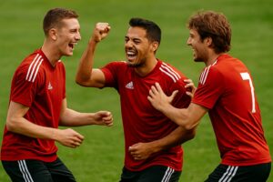 サッカーの練習中、赤いユニフォームの選手たちが笑顔で声を掛け合い、拳を上げている様子