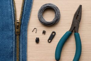 ファスナー修理に使う工具や交換用パーツがテーブルに整理されて並べられている様子。小物入れや定規も添えられている。