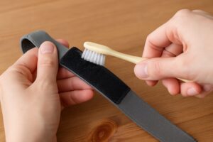 歯ブラシを使ってマジックテープの表面に絡んだホコリを取り除いている様子。修復作業中の手元がアップで写っている。