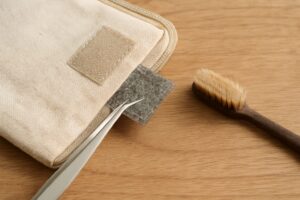 ベージュのポーチに付いたマジックテープを、ピンセットと歯ブラシで手入れしている様子。