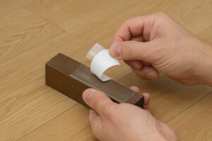 木製の棚の下に滑り止めテープを貼り付けている様子。作業中の手元がアップで写っている。