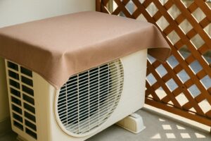 屋外に設置された室外機の上に、アルミ製の日よけカバーが取り付けられている様子。
