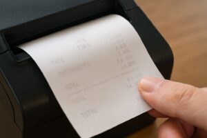 感熱紙のレシートがプリンターから出てくる様子。指で紙を押さえている。