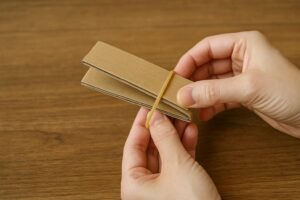 折りたたんだ厚紙に輪ゴムをかけて簡易的な挟み道具を作っている手元の様子。