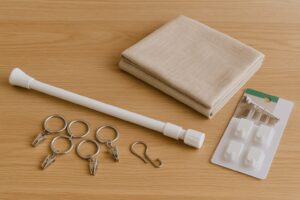 カーテン仕切りに使える100円ショップのアイテム。突っ張り棒、カーテンリング、軽量布、フックなどがテーブルにきれいに並べられている様子。