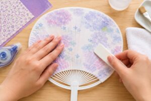 うちわの骨組みに紙を中央から丁寧に貼りながら、シワができないよう作業している様子