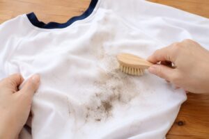 泥汚れが付いた白い体操服をブラシでやさしく払い、表面の泥を落としている様子