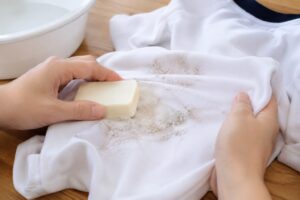 泥汚れが付いた白い体操服に固形石けんを塗り込み、部分洗いをしている様子