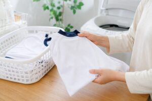 洗濯後のきれいな白い体操服をたたみ、洗濯かごの横で整えている様子